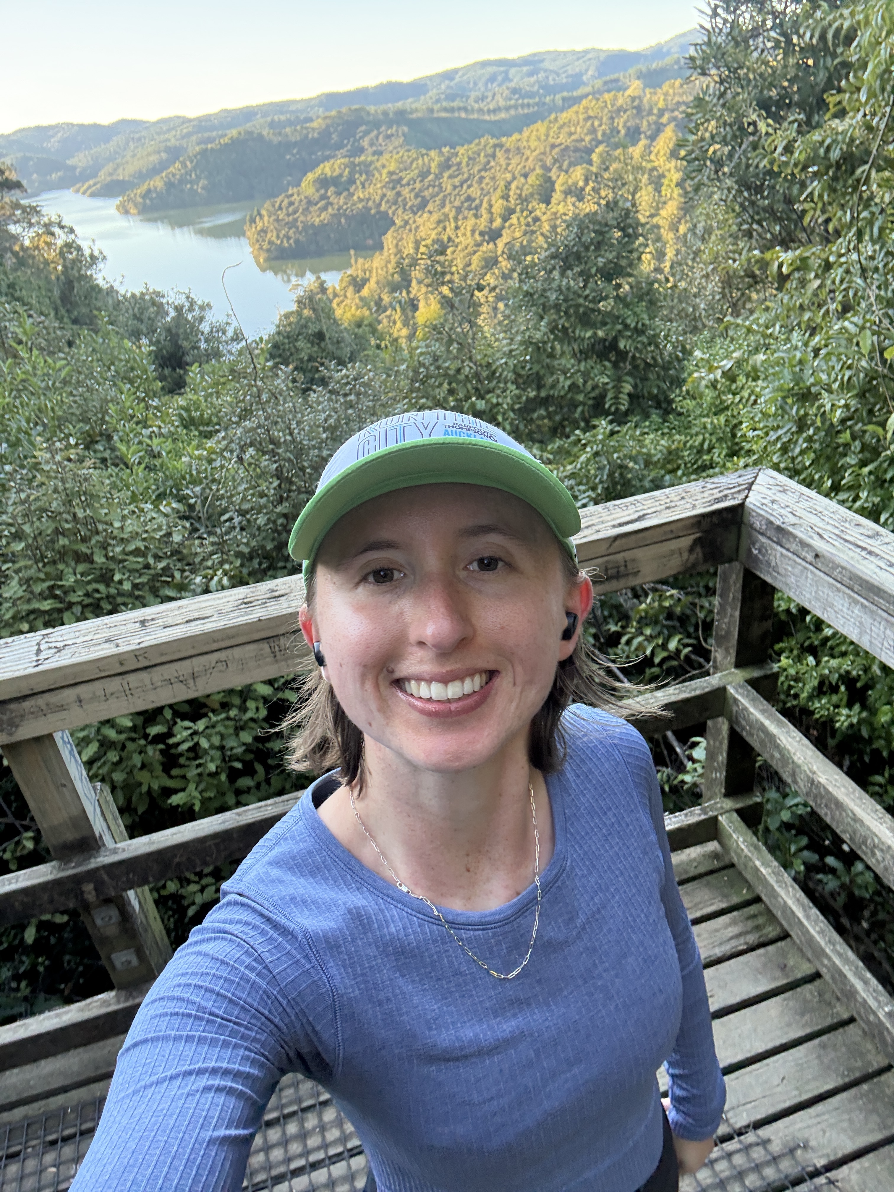 Person in a green cap takes a selfie in front of a lush green landscape.