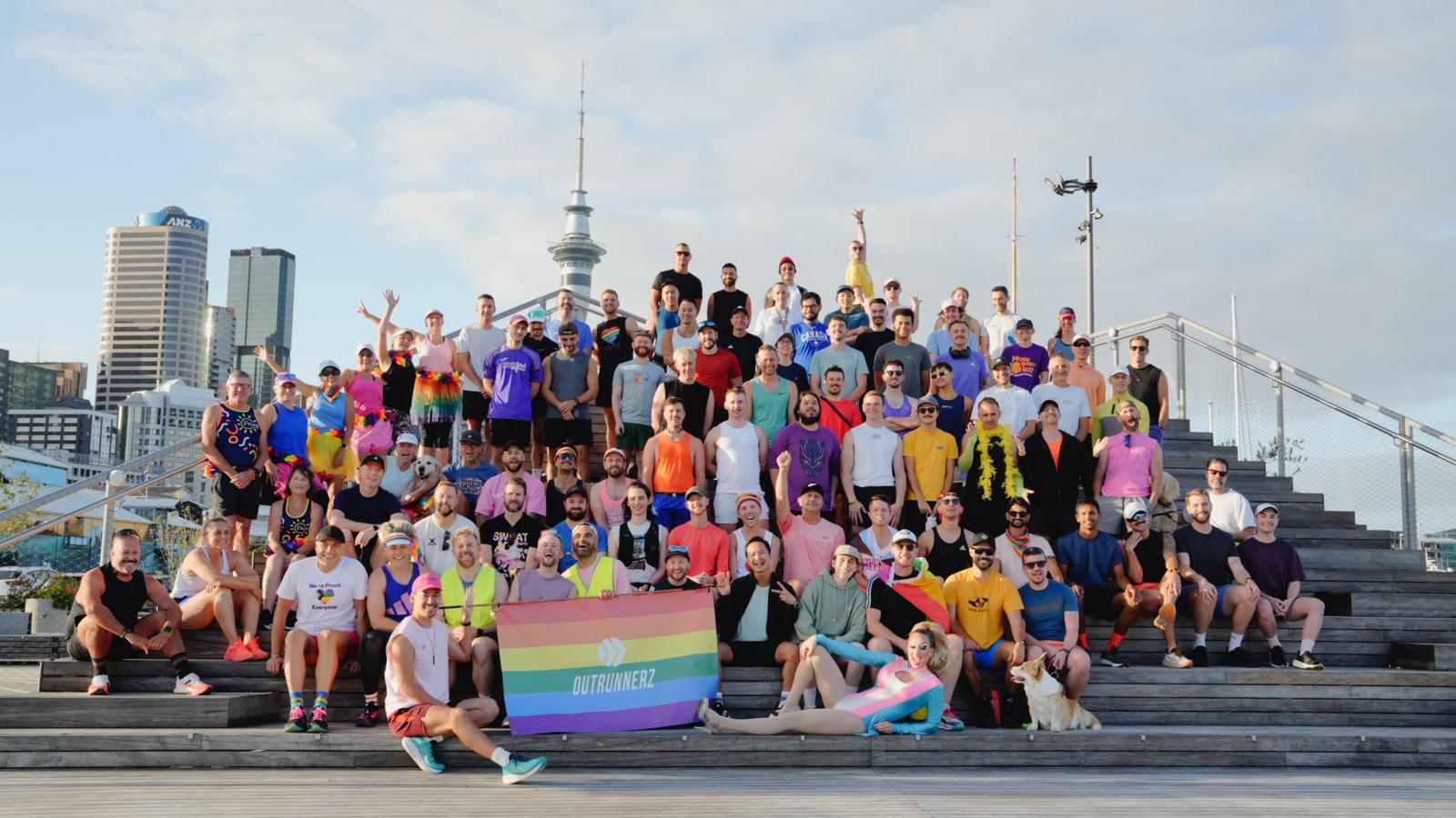 Big group of runners in active wear posing for a photo, the Auckland Sky Tower is in the background.