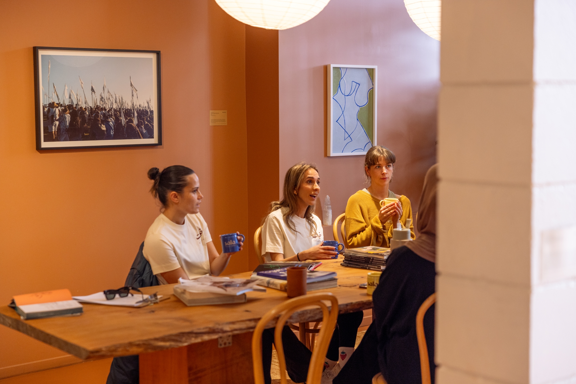 A group of people at a table having a discussion, in a warmly lit room with photos and art on the walls.