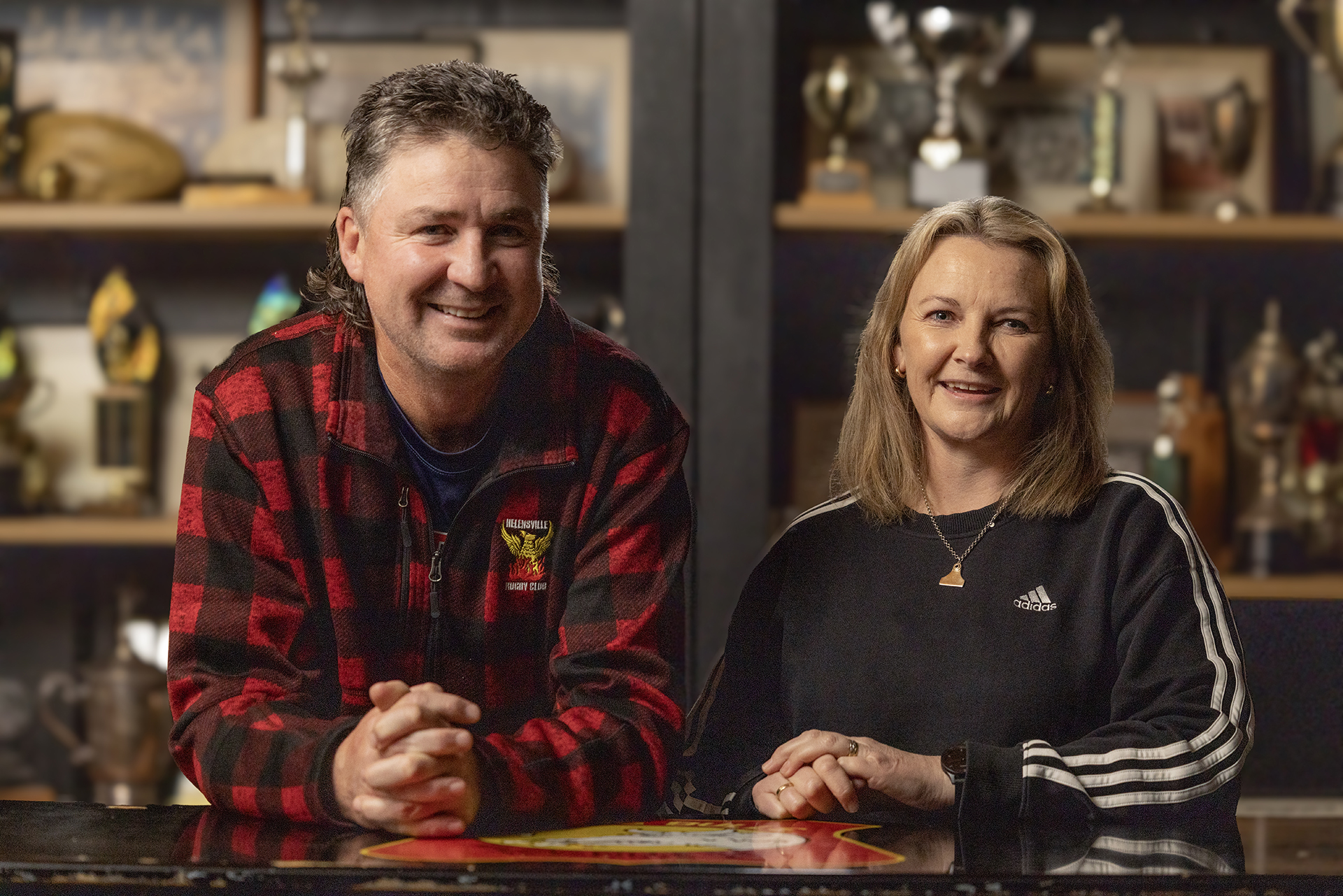 Two people in front of trophy-lined shelves, posing for a portrait behind a table.