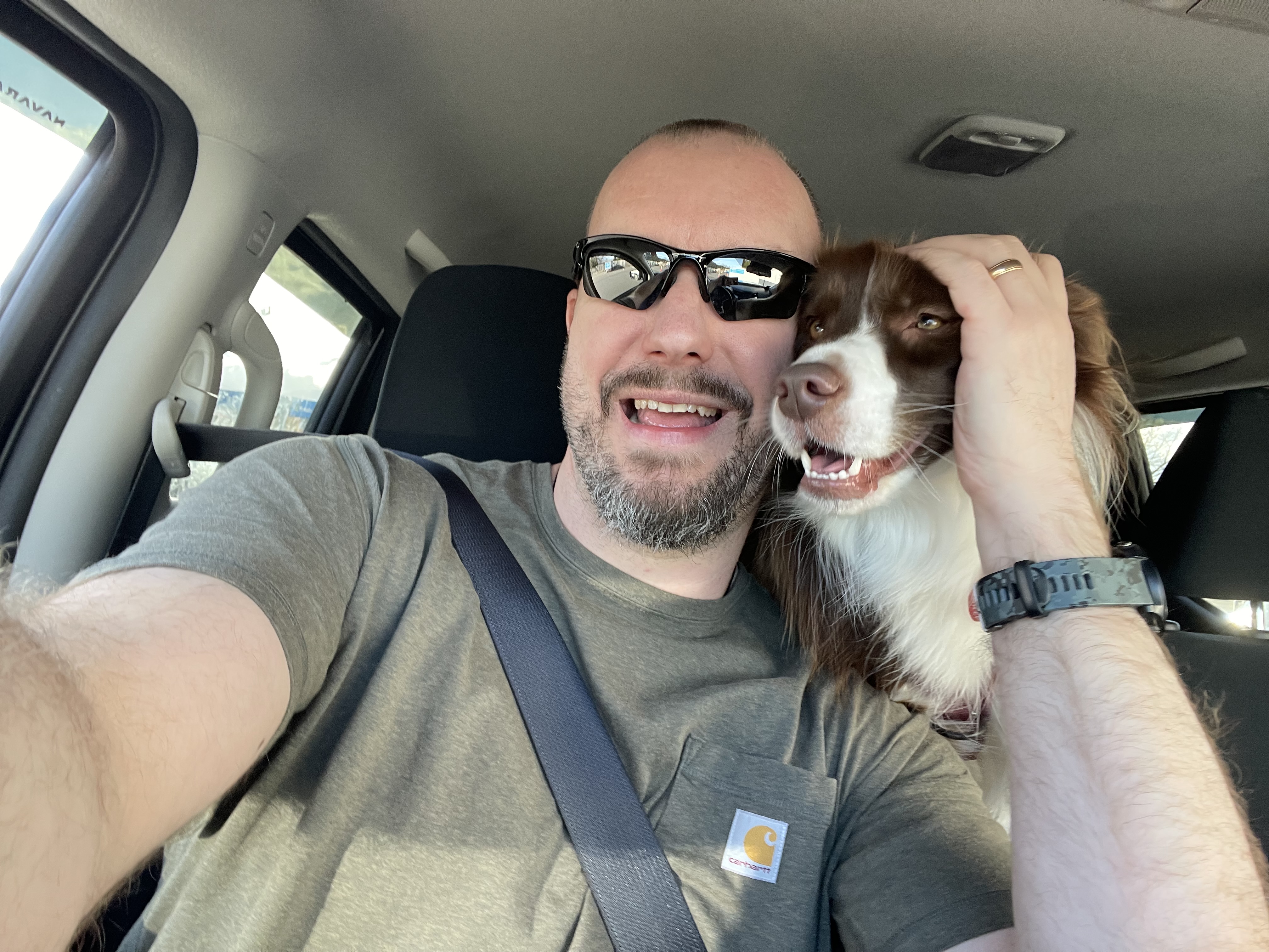 Person in the driver's seat of a car cuddles a dog that's in the back seat. 