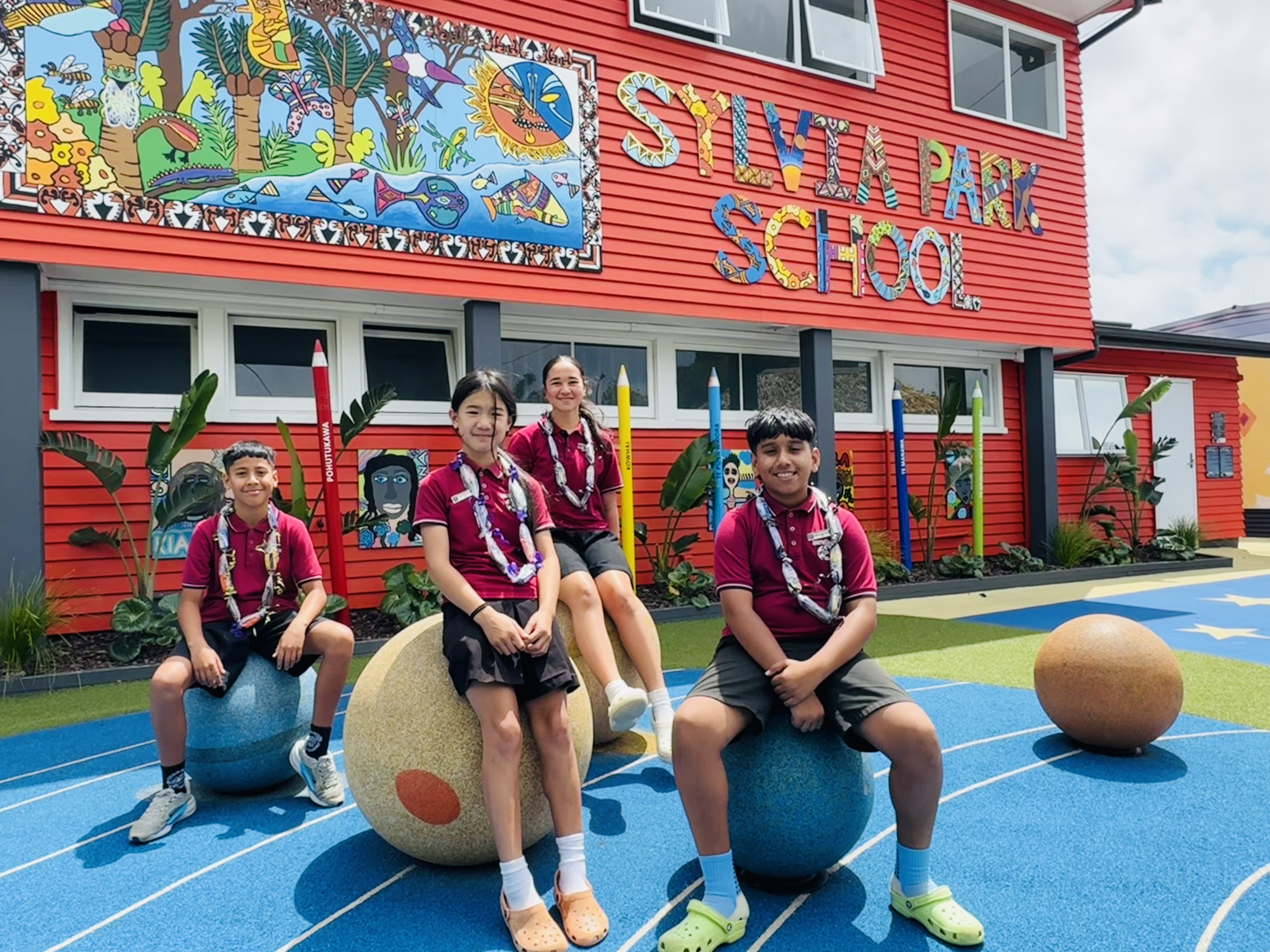 Students pose in front of a red school building of Sylvia Park School.