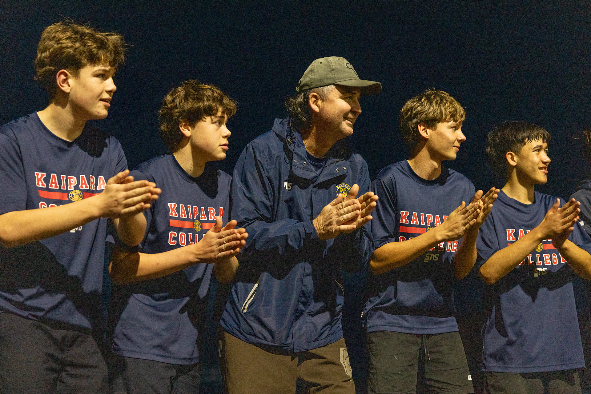 Coach and rugby players applaud on the sideline during an evening training session.