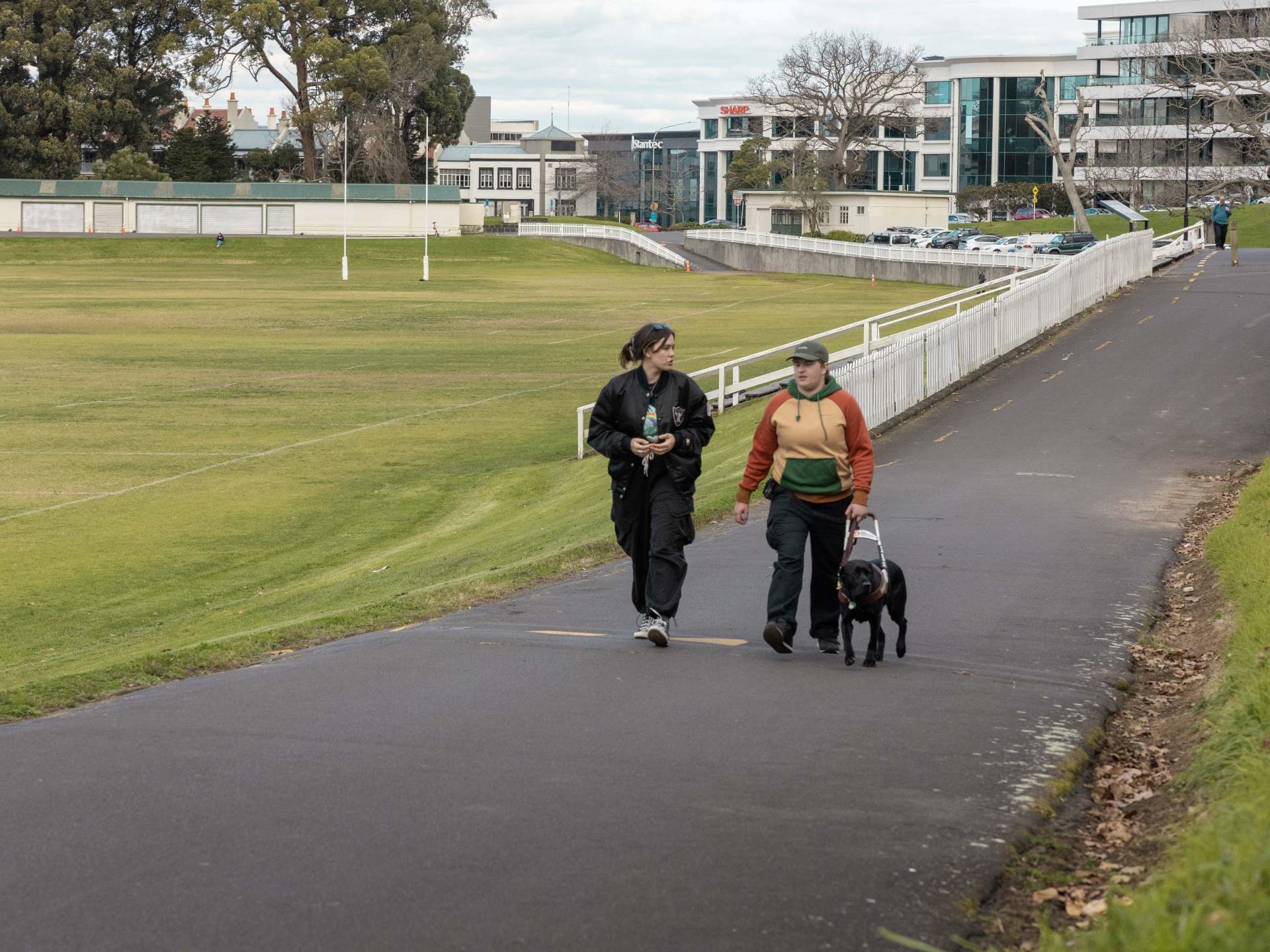 Two people walk along a path in a domain, one of them with their black Labrador guide dog.
