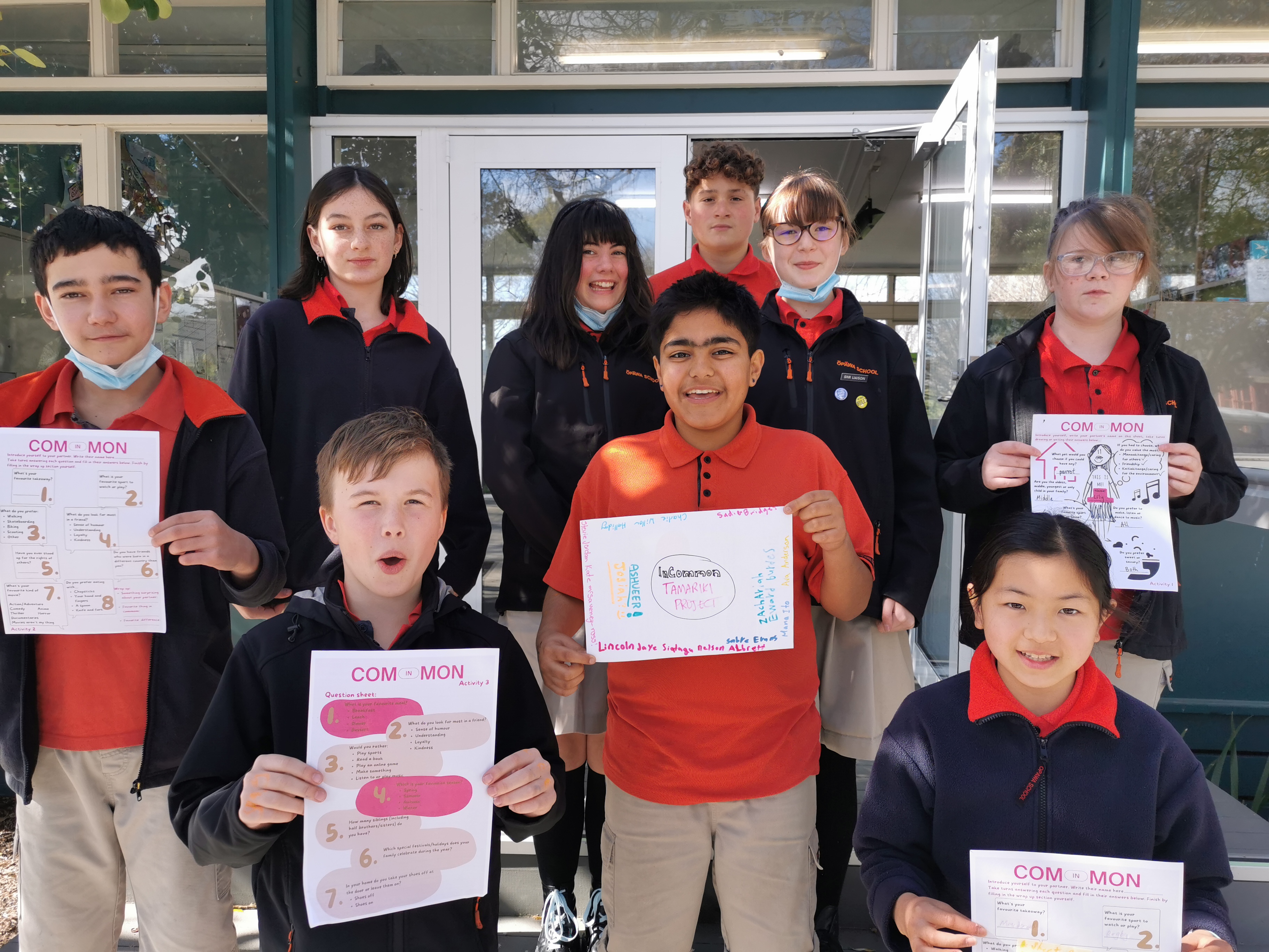 School students holding up hand-drawn InCommon posters outside a school building as part of a diversity and inclusion learning activity.